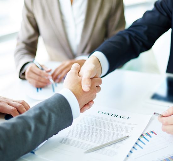 Image of business partners handshaking over business objects on workplace